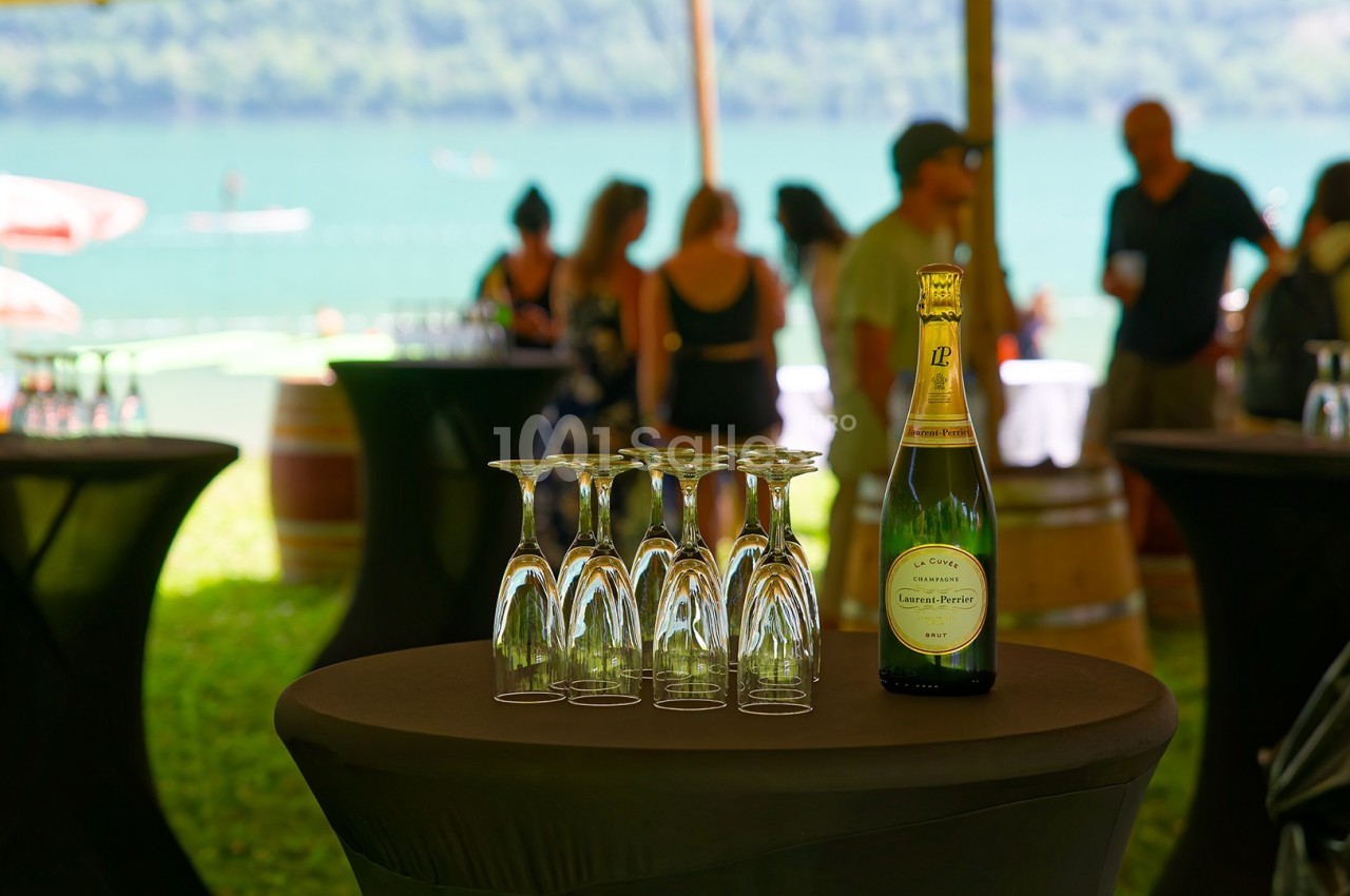 Bouteille de champagne et verres retournés sur une table lors d'un événement en extérieur près d'un lac.