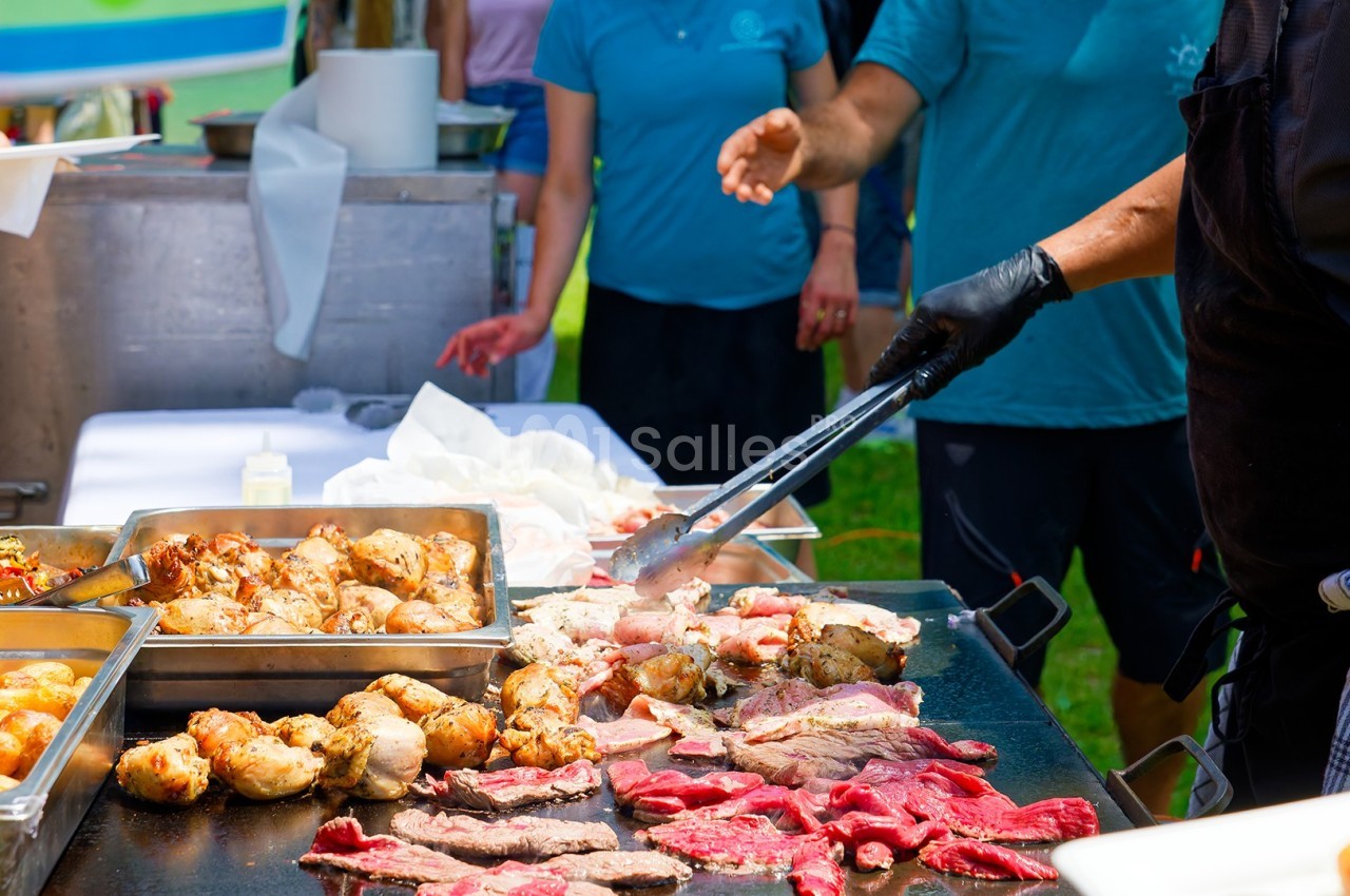Personne préparant de la viande grillée sur une plaque chauffante lors d'un événement en plein air.