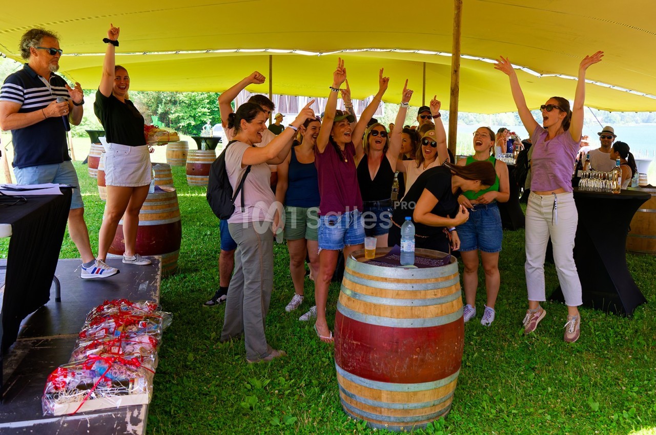 Un groupe de personnes enthousiastes célèbre sous une tente, entouré de tonneaux et d'éléments festifs en extérieur.