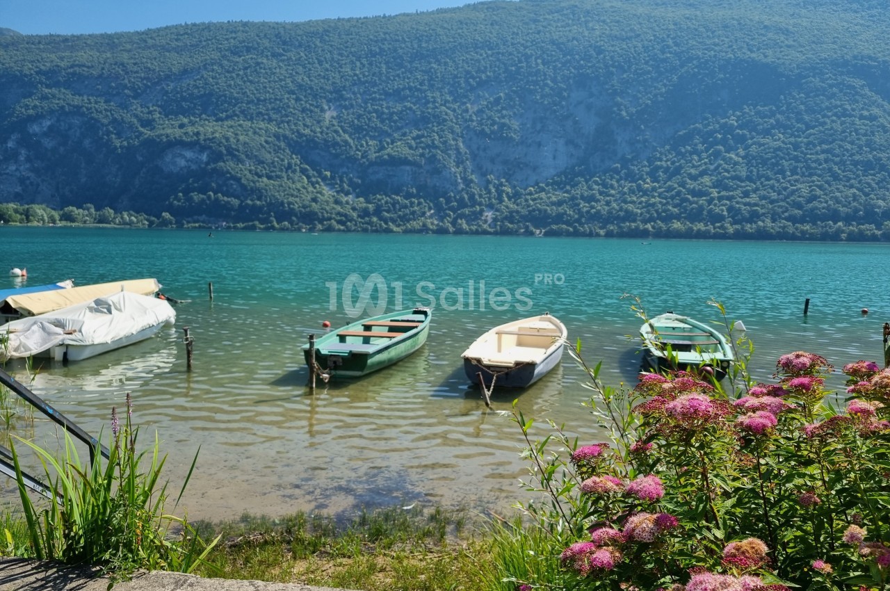 Quatre barques amarrées sur un lac turquoise entouré de montagnes verdoyantes, avec des fleurs au premier plan.