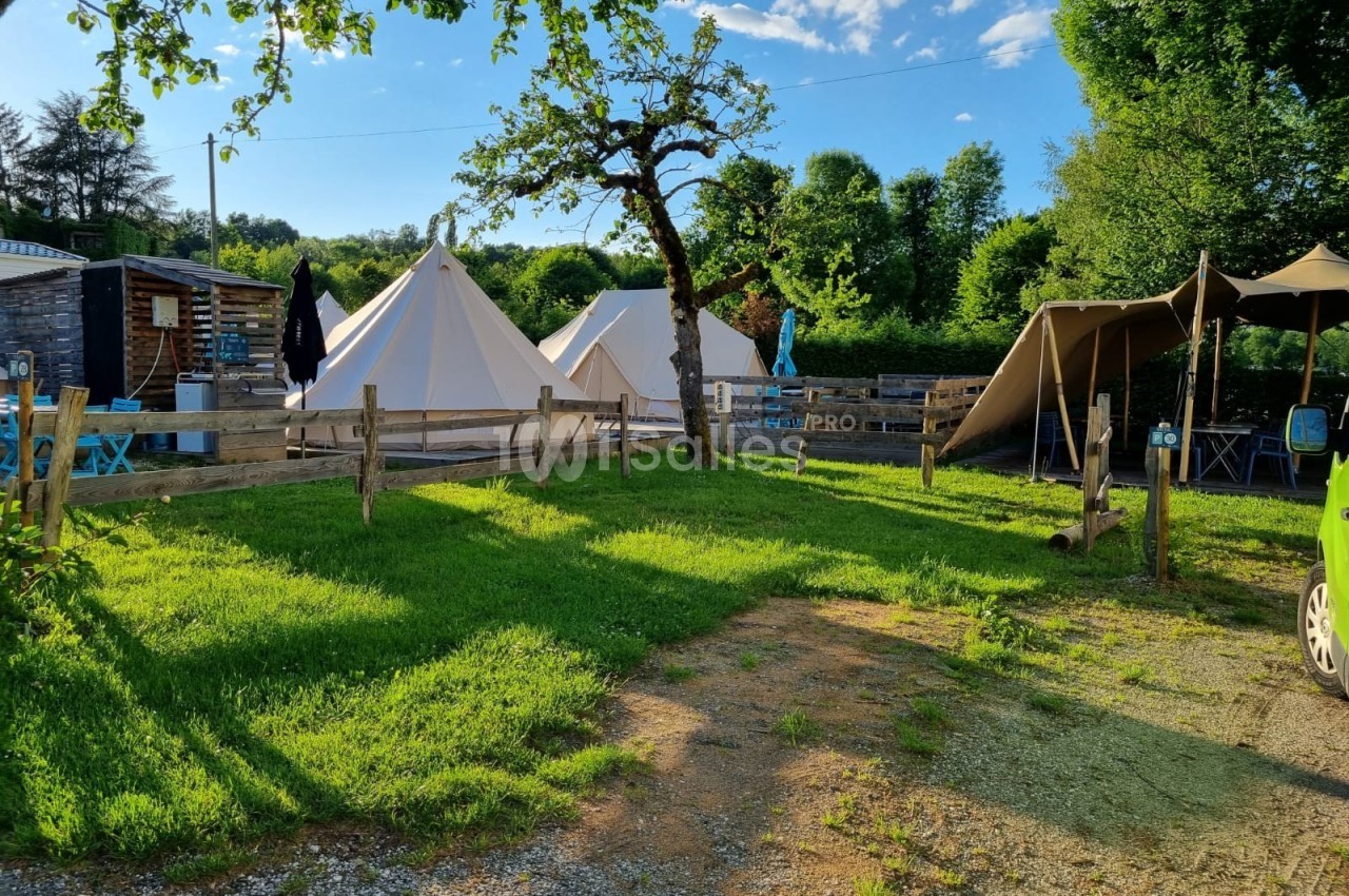 Tentes blanches installées dans un espace verdoyant avec arbres, clôtures en bois et mobilier extérieur.