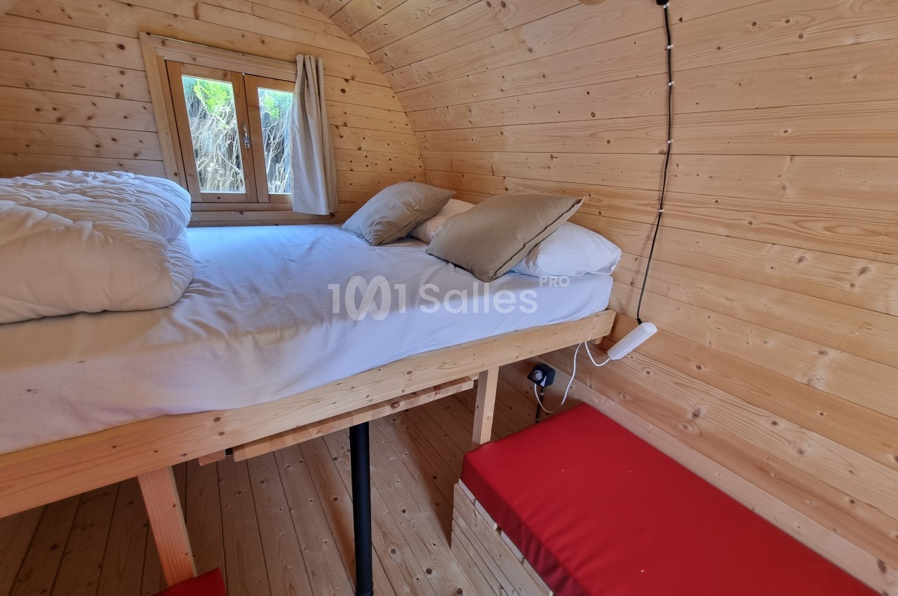 Intérieur d'une petite chambre en bois avec un lit surélevé, des coussins, une fenêtre et un banc rouge.