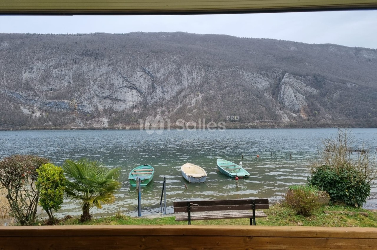 Vue sur un lac calme avec quatre barques amarrées, entouré de montagnes et de végétation en hiver.