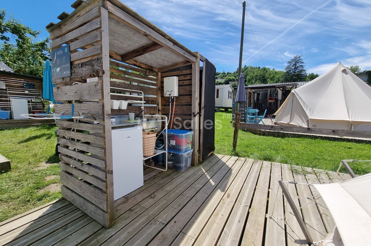 Cuisine extérieure en bois avec évier, réfrigérateur et étagères, située sur une terrasse en bois dans un camping.