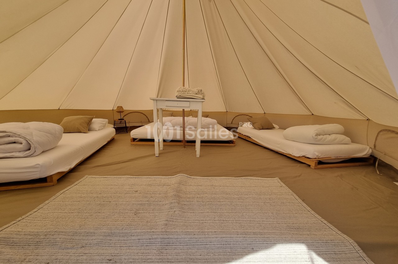 Intérieur d'une tente spacieuse avec lits simples, table centrale, tapis clair et lumière naturelle.