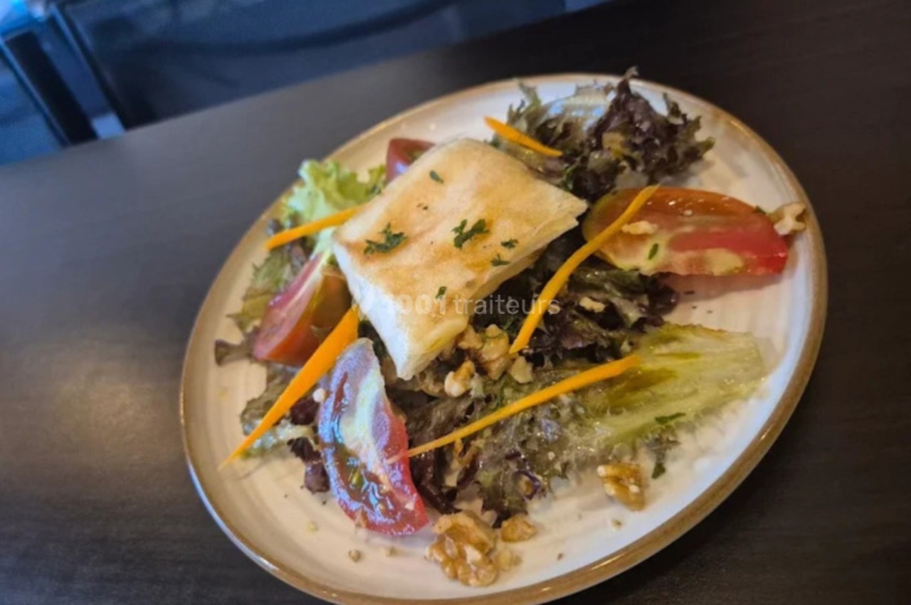 Assiette de salade composée avec fromage grillé, tomates, carottes, noix et feuilles de salade sur une table sombre.