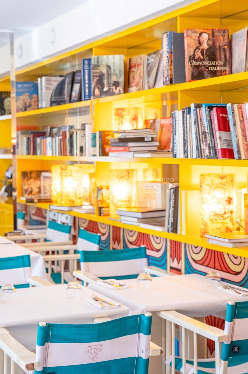 Salle de restaurant lumineuse avec étagères jaunes remplies de livres et tables dressées avec chaises pliantes.
