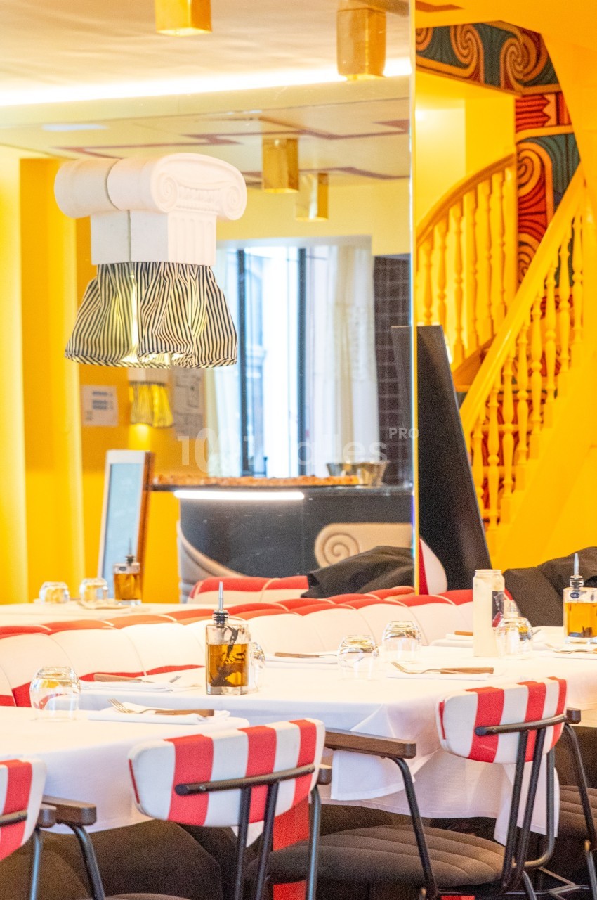 Salle de restaurant lumineuse avec tables dressées, chaises rayées rouges et blanches, et décorations murales colorées.