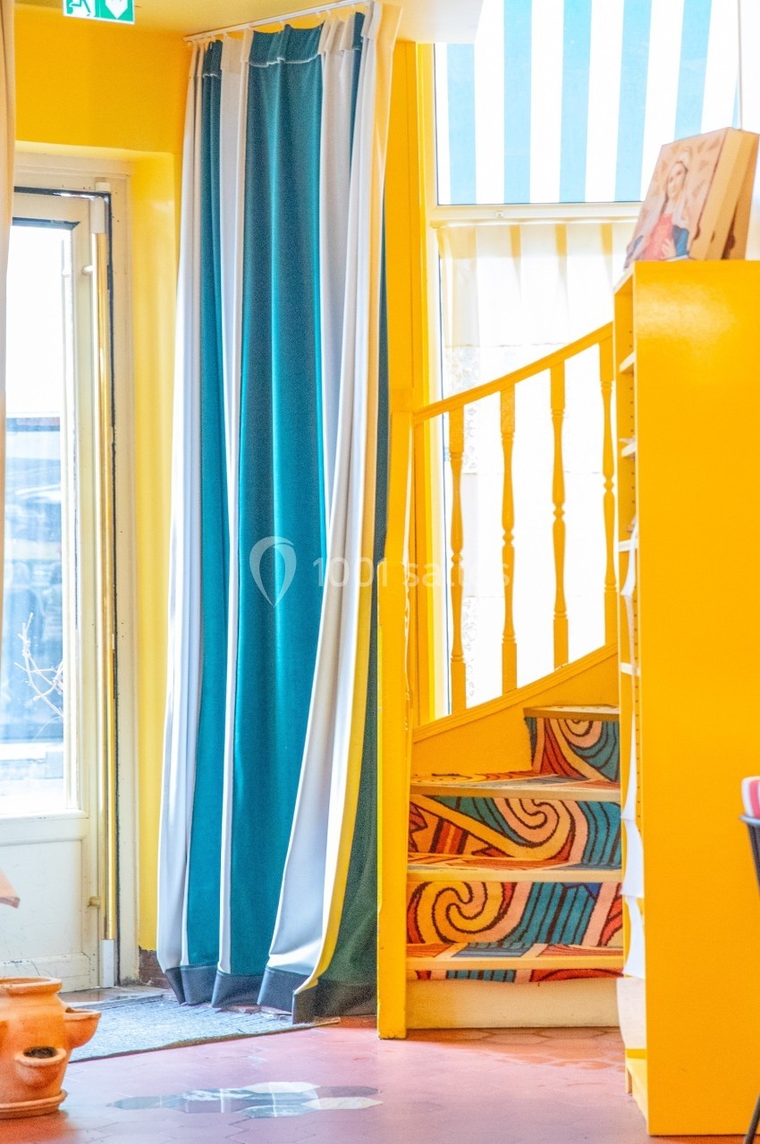 Escalier jaune avec motifs colorés, entouré de rideaux bleus et blancs dans un intérieur lumineux.