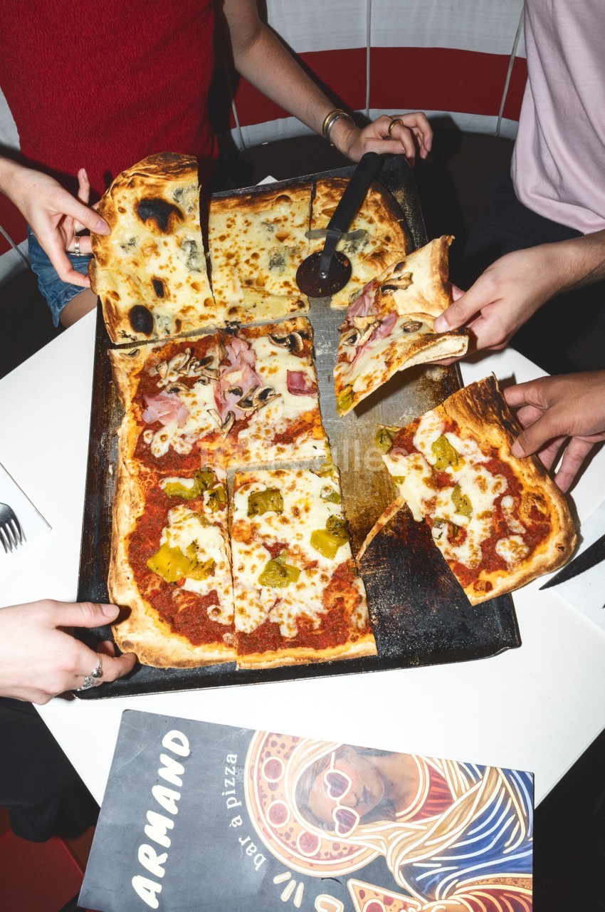 Plusieurs personnes partagent une pizza découpée en parts sur une planche noire.