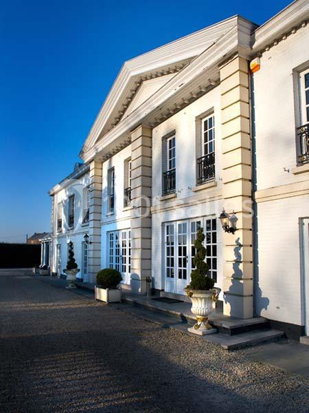 Façade d'un grand bâtiment blanc de style classique avec colonnes, fenêtres à carreaux et allée gravillonnée.