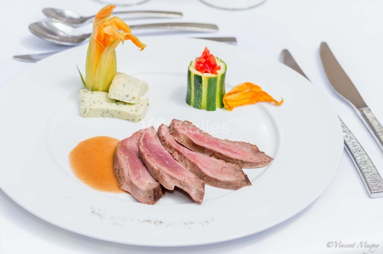 Assiette gastronomique avec tranches de viande, sauce, courgette farcie et fleur comestible en décoration.