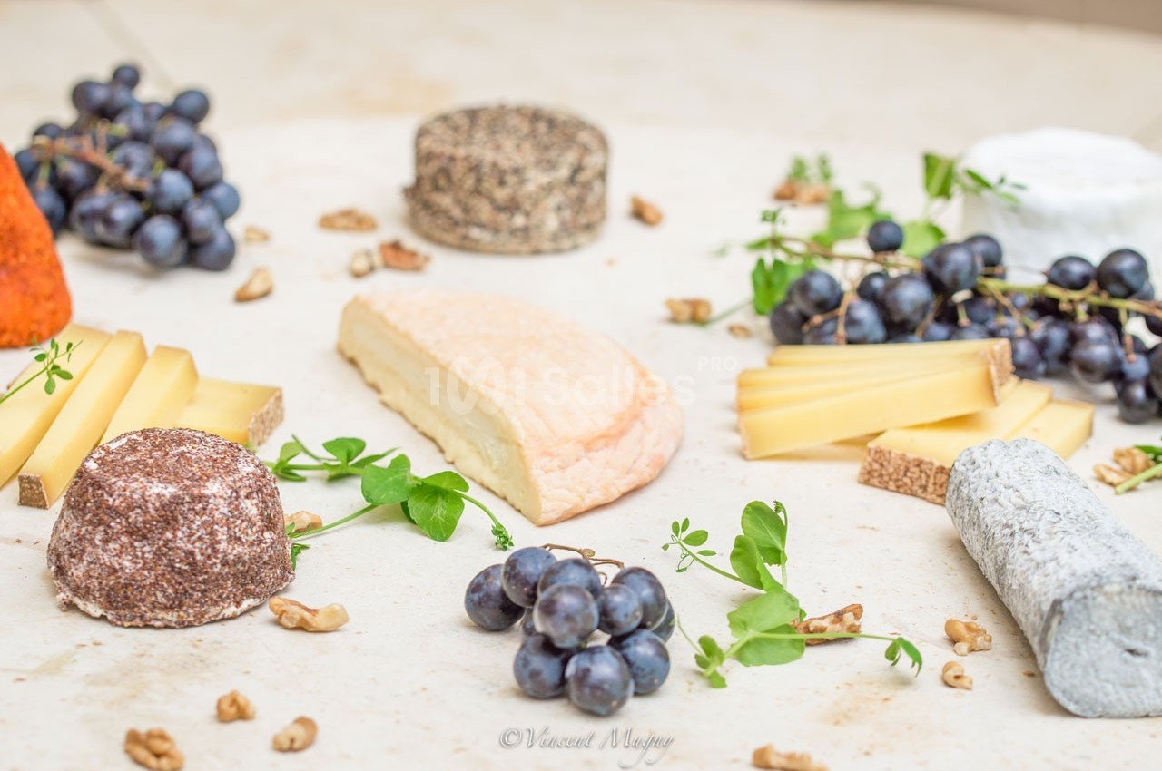 Plateau de fromages variés entourés de grappes de raisin, noix et herbes fraîches sur une table claire.