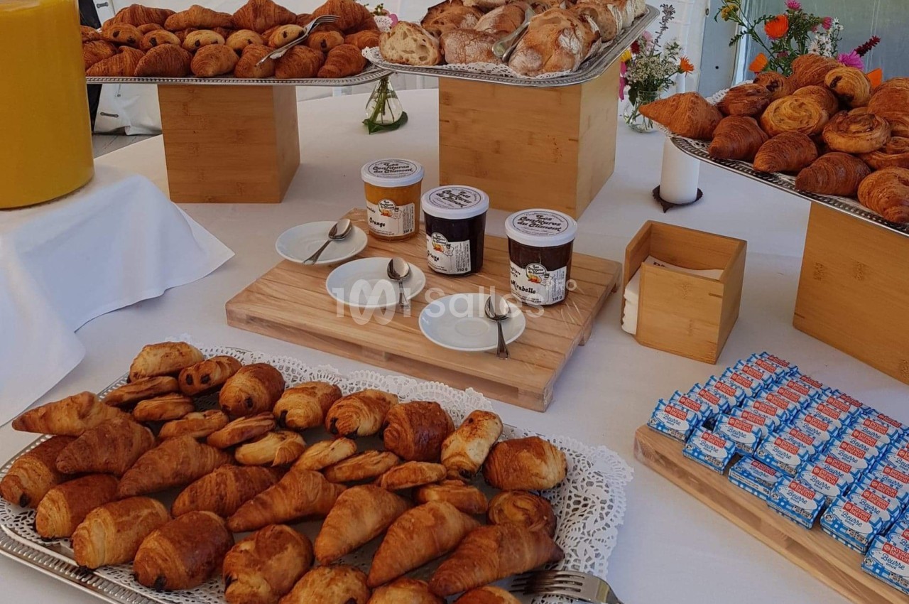 Plateau de viennoiseries variées avec confitures, jus d'orange et décor floral sur une table dressée.