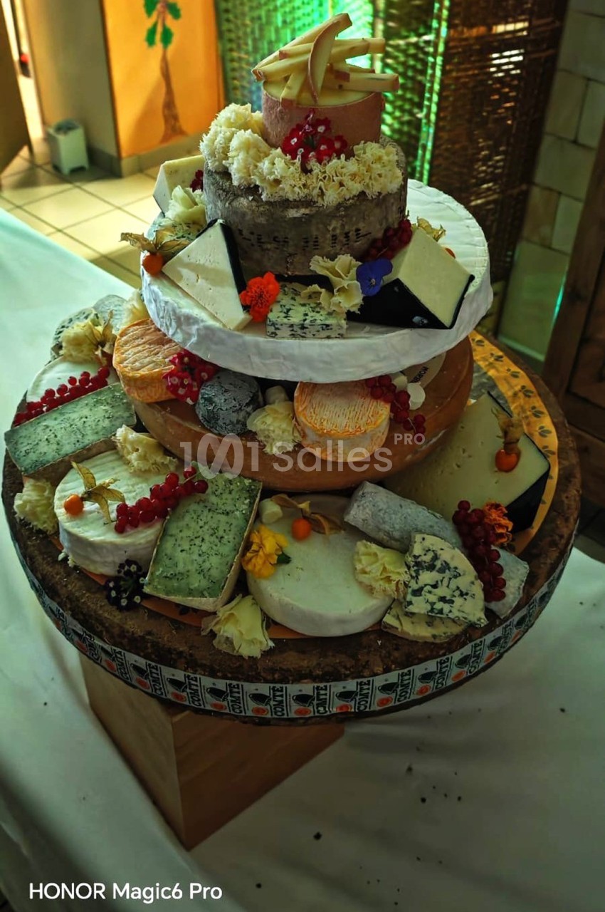 Plateau de fromages variés disposés en forme de pièce montée, décoré de fruits rouges et de fleurs comestibles.