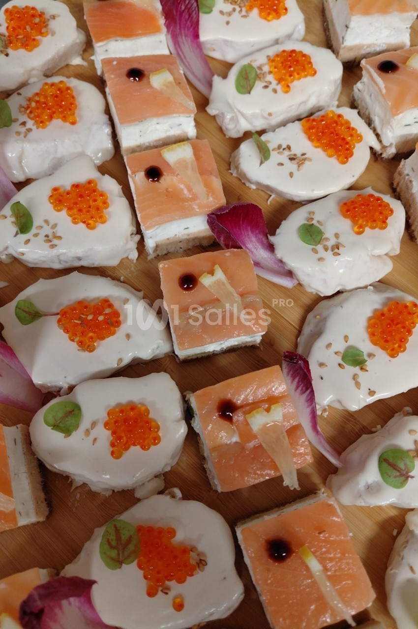 Assortiment de bouchées apéritives avec saumon fumé, œufs de poisson, crème et décorations florales.