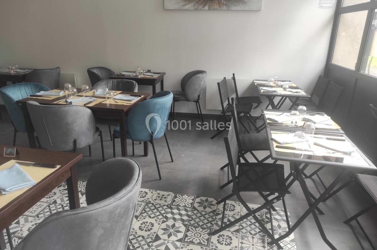 Salle de restaurant lumineuse avec tables dressées, chaises variées et sol en carreaux de ciment décoratifs.