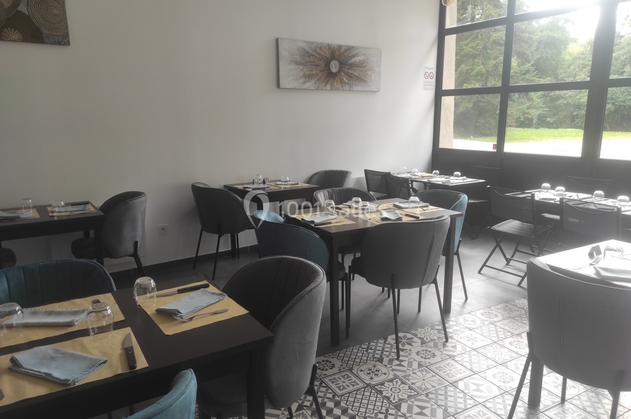 Salle de restaurant lumineuse avec tables dressées, chaises modernes et grandes fenêtres donnant sur un espace vert.