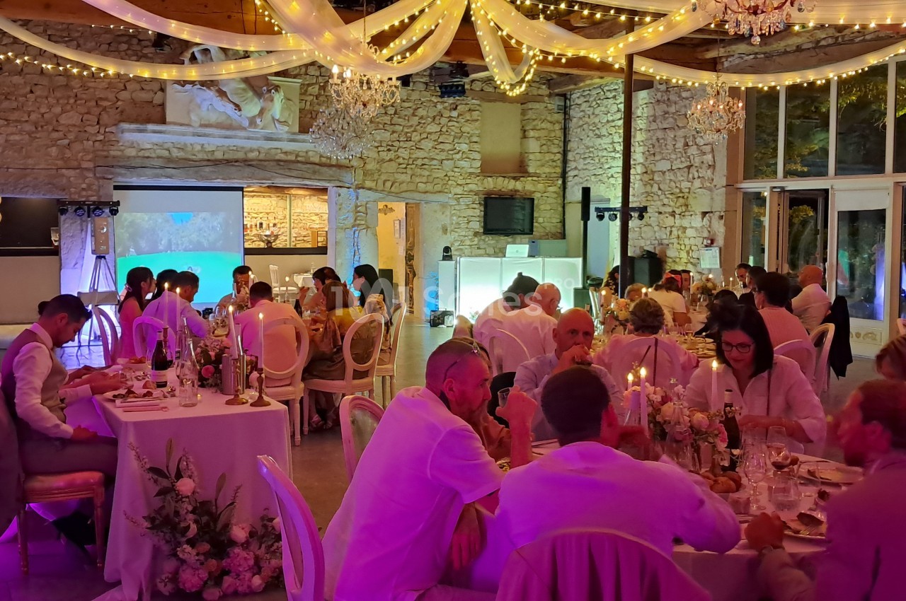 Salle de réception en pierre éclairée par des lumières tamisées, avec des invités assis à des tables décorées.