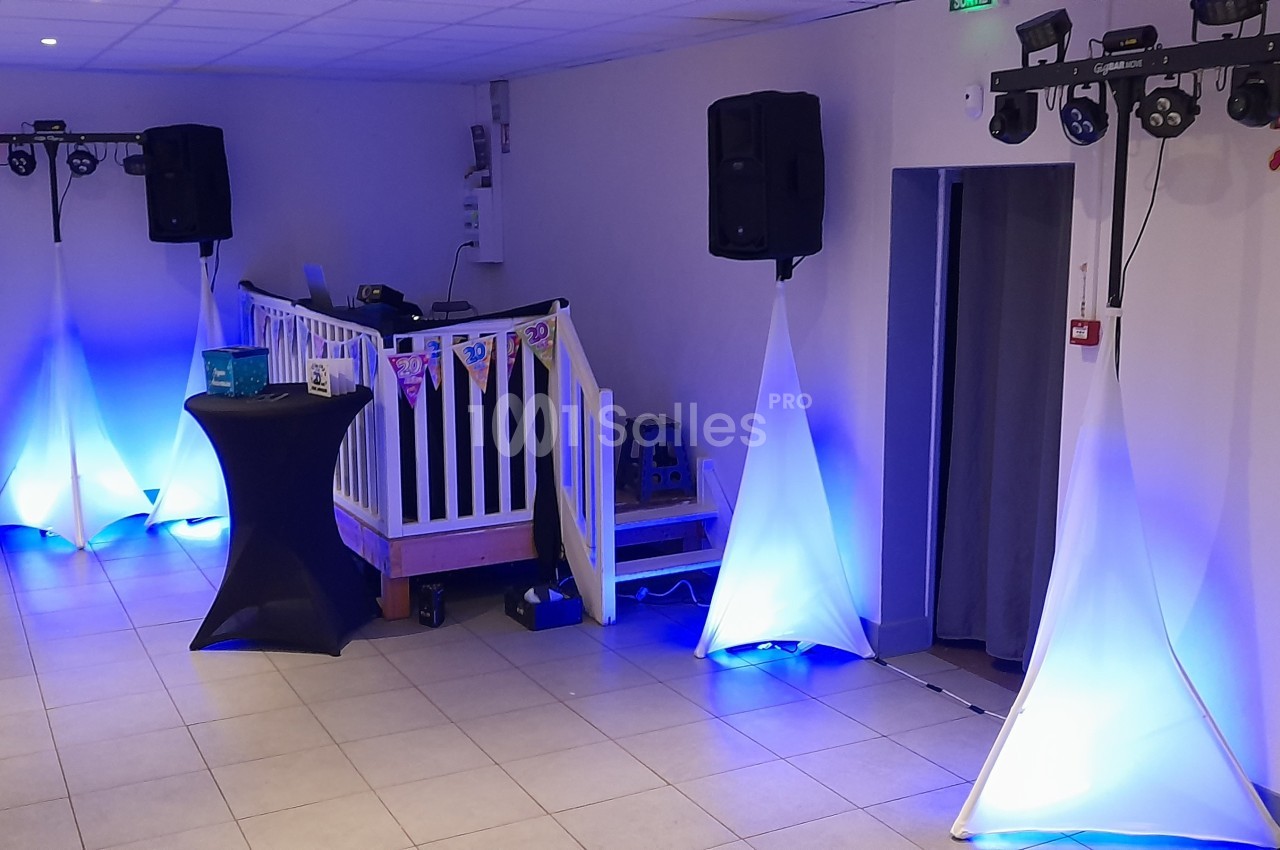 Salle décorée pour un événement avec éclairages bleus, ballons blancs et bleus, et une petite estrade.