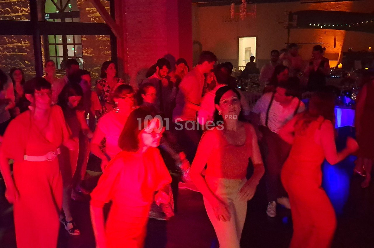 Des personnes dansent dans une salle faiblement éclairée avec des lumières rouges et une ambiance festive.