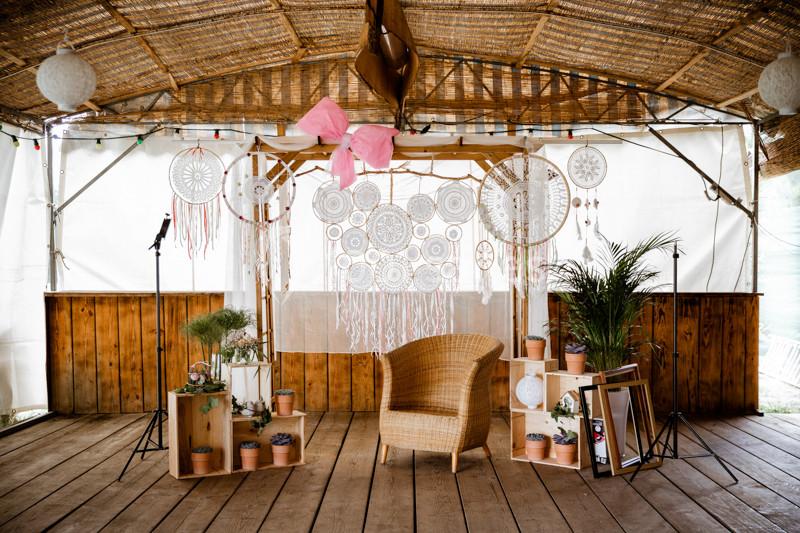 Décoration bohème avec fauteuil en osier, attrape-rêves suspendus, plantes en pots et éléments en bois sous une structure…