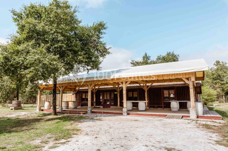Bâtiment en bois avec toit clair, entouré d'arbres, situé dans un espace extérieur dégagé.