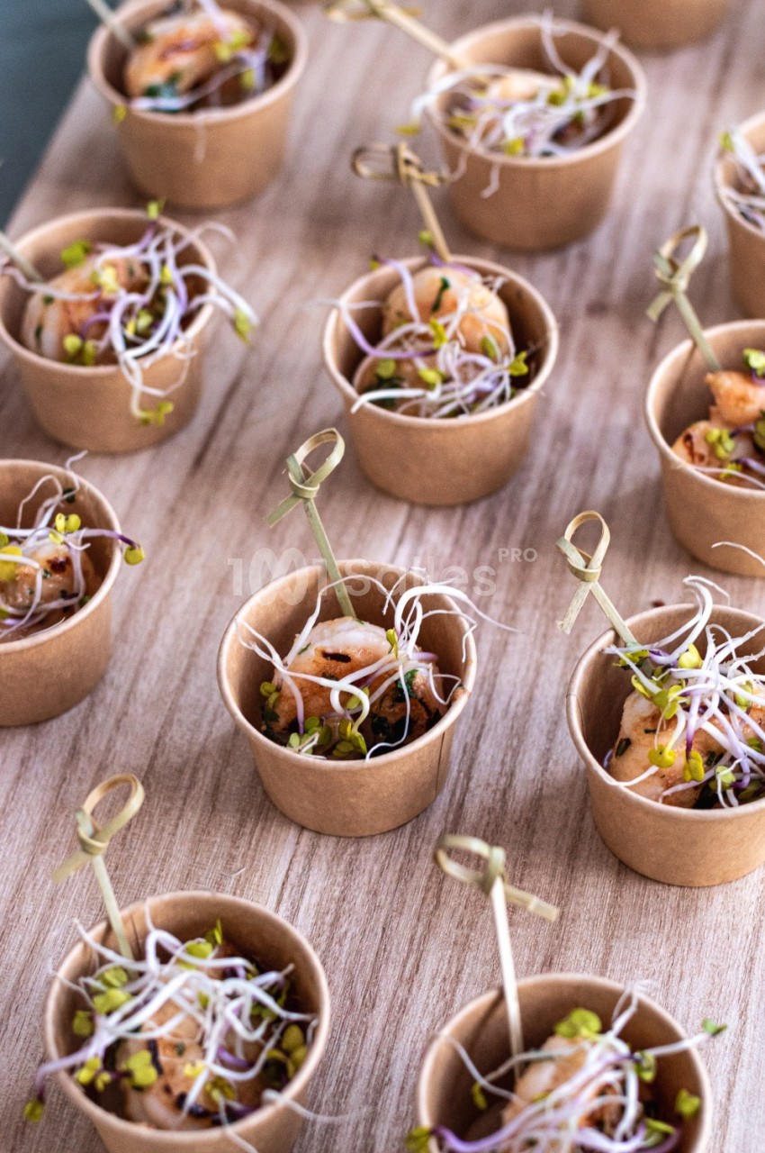 Petits pots en carton contenant des bouchées garnies de crevettes, pousses germées et herbes fraîches, présentés sur une…