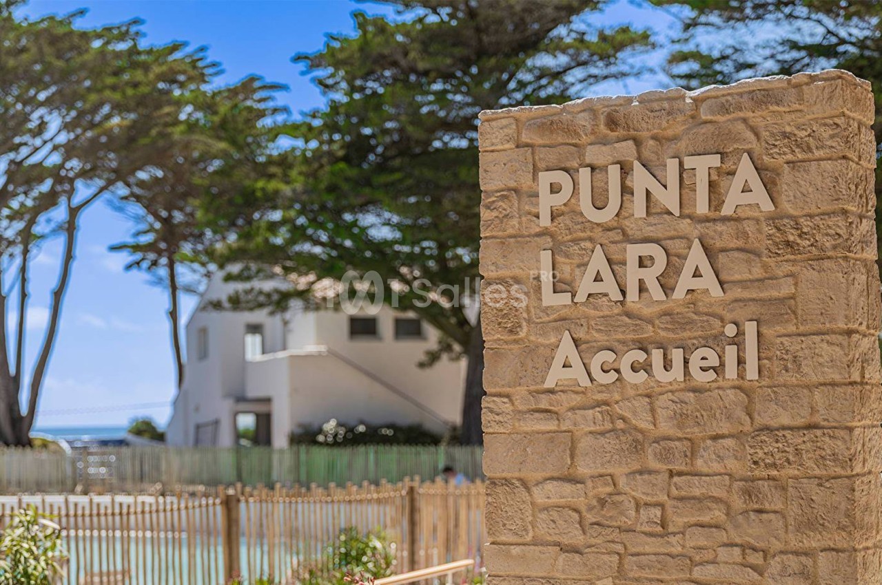 Panneau en pierre indiquant ’Punta Lara Accueil’ devant un bâtiment blanc entouré d'arbres et de végétation.