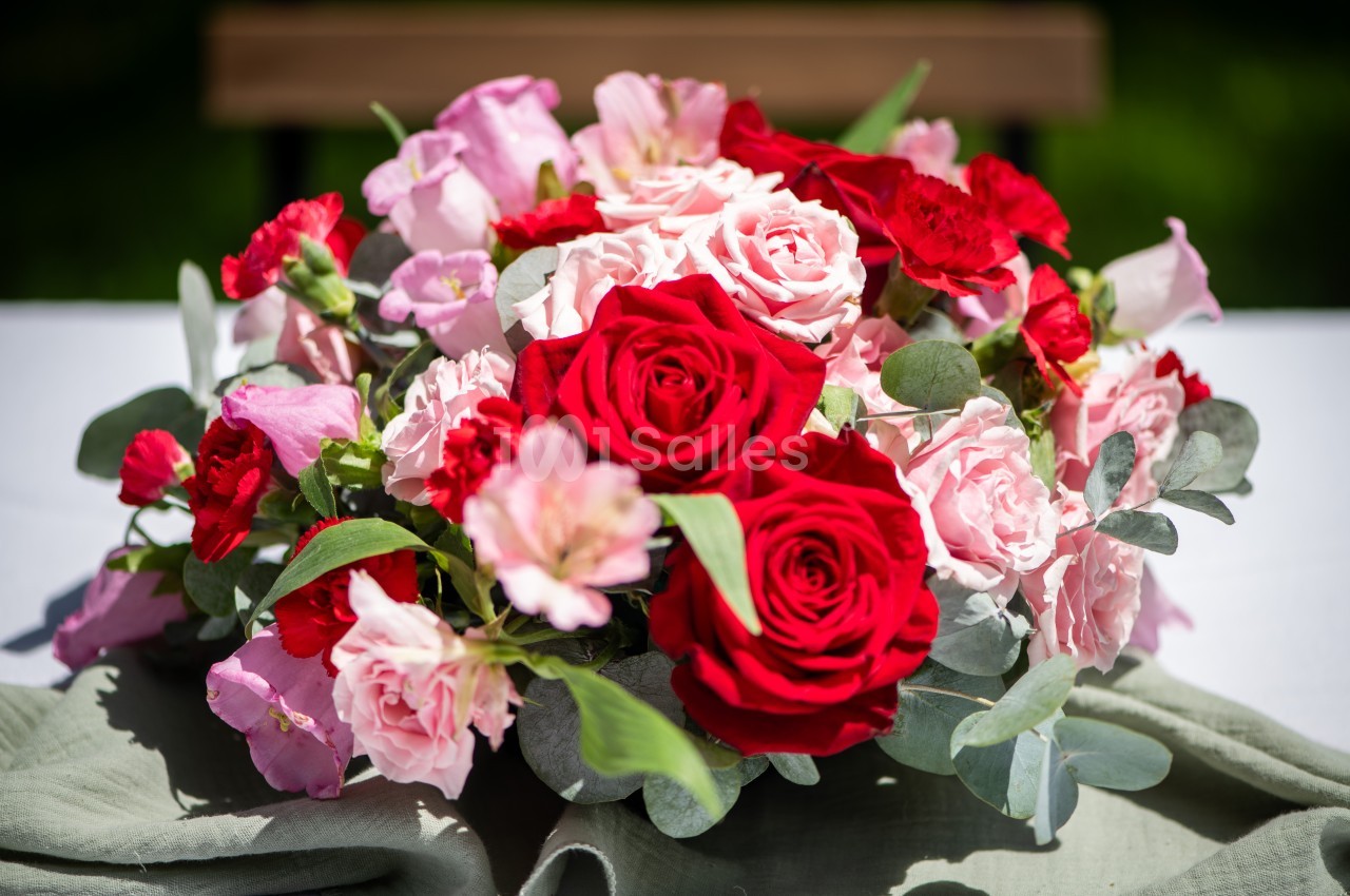 Bouquet de fleurs composé de roses rouges, roses pâles et feuillage vert, posé sur une nappe blanche.