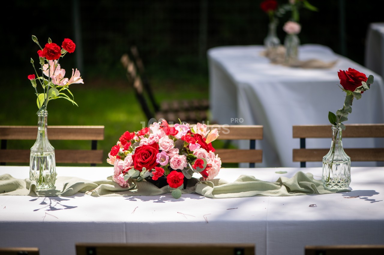 Table décorée avec un bouquet de fleurs rouges et roses, entourée de vases assortis, en extérieur.
