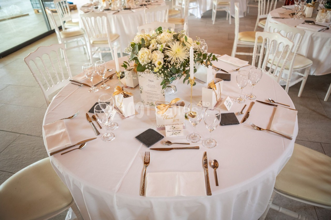 Table de réception élégamment dressée avec nappes blanches, couverts dorés, centre de table floral et menus personnalisés.