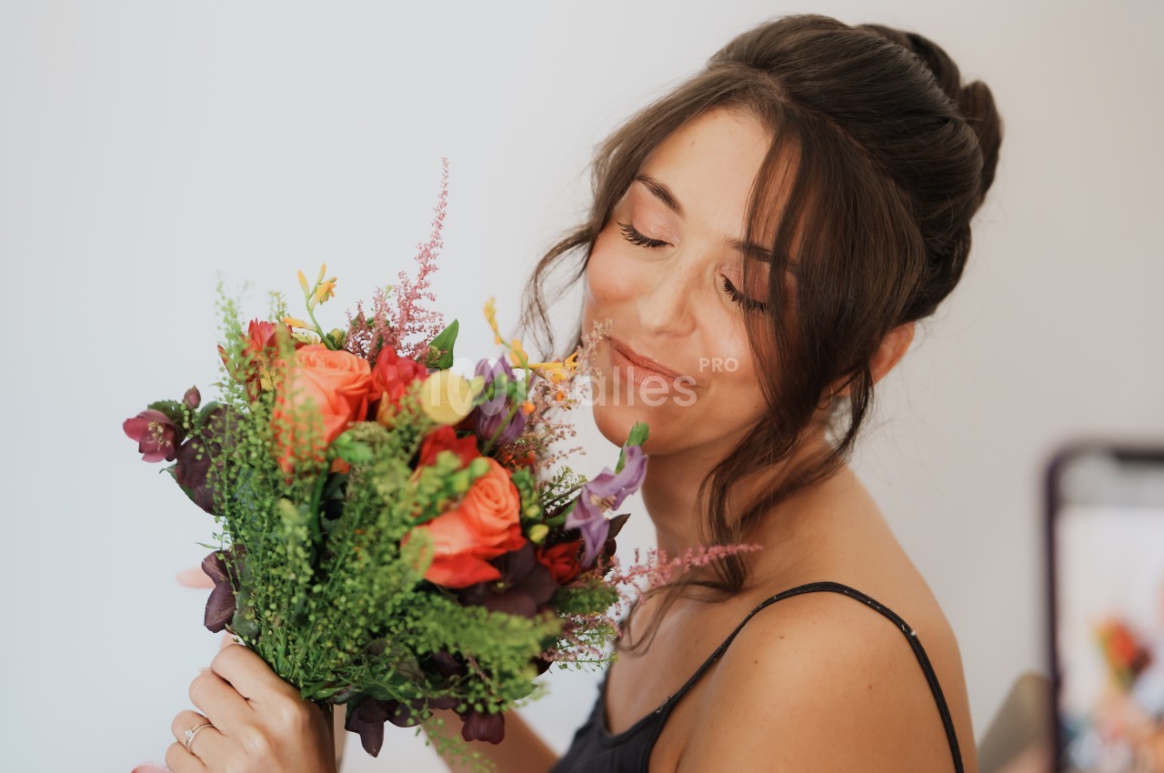 Femme souriante tenant un bouquet de fleurs colorées, dans un cadre lumineux et épuré.