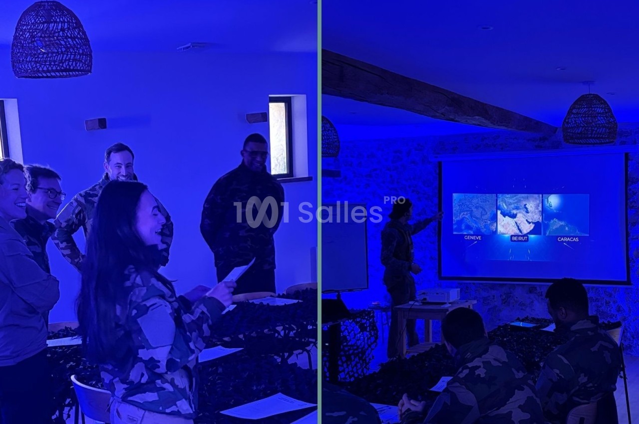 Des personnes en tenue militaire assistent à une présentation dans une salle éclairée par une lumière bleue.