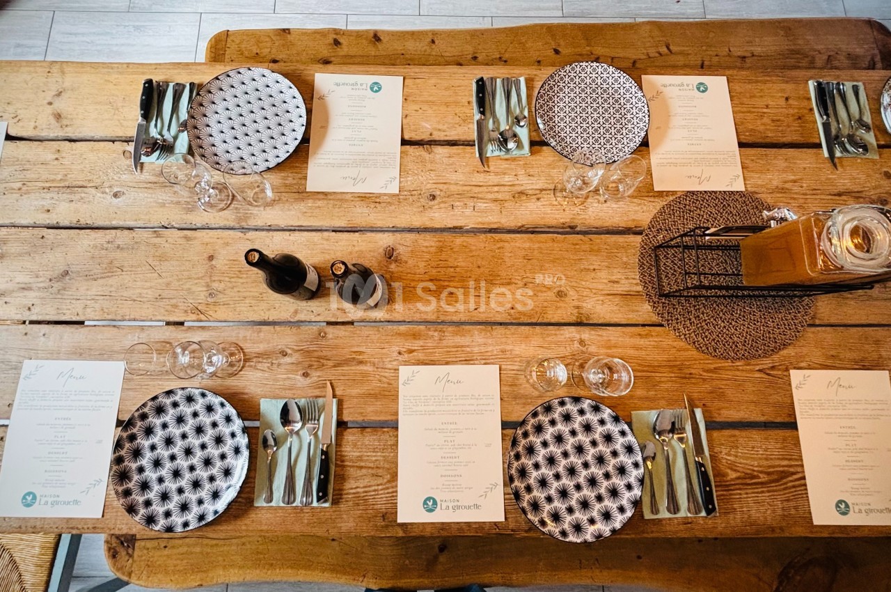 Table en bois dressée avec des assiettes à motifs, couverts, verres, menus et un centre de table décoratif.