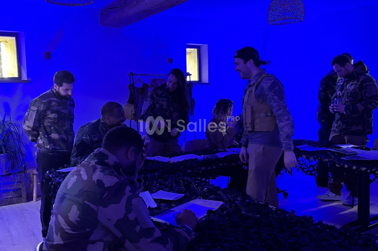 Des personnes en tenue militaire participent à une activité de groupe dans une pièce éclairée par une lumière bleue.