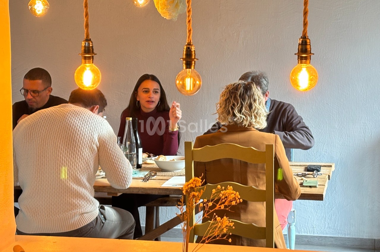 Quatre personnes discutent autour d'une table dans un restaurant éclairé par des ampoules suspendues.
