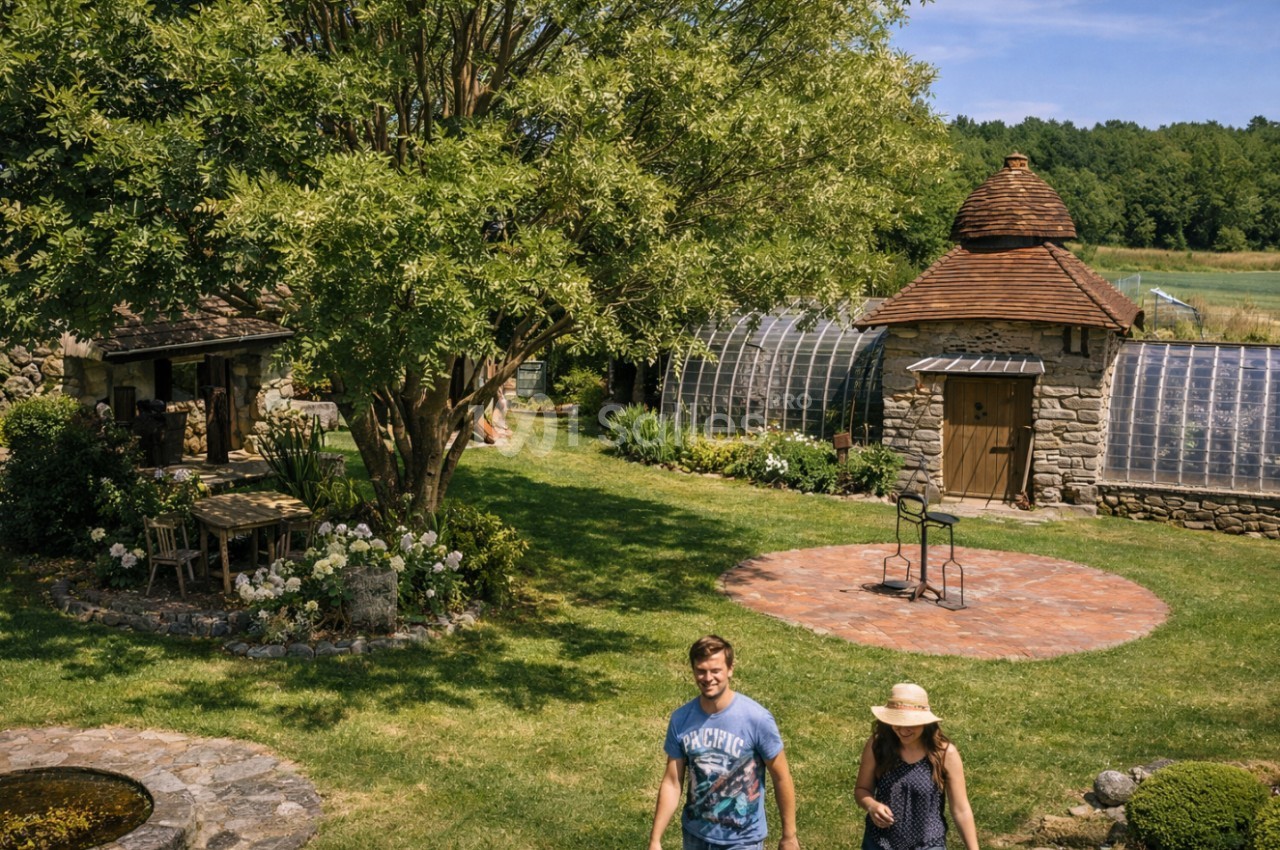 Un jardin verdoyant avec des serres, une petite maison en pierre et deux personnes marchant sur une pelouse.