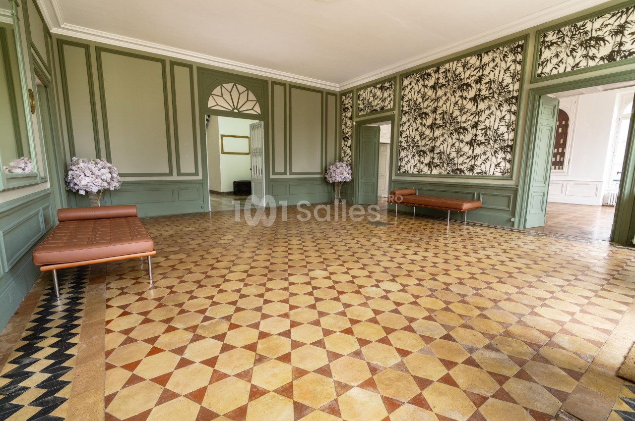 Salle lumineuse avec carrelage géométrique, murs verts, bancs en cuir et décorations florales aux angles.