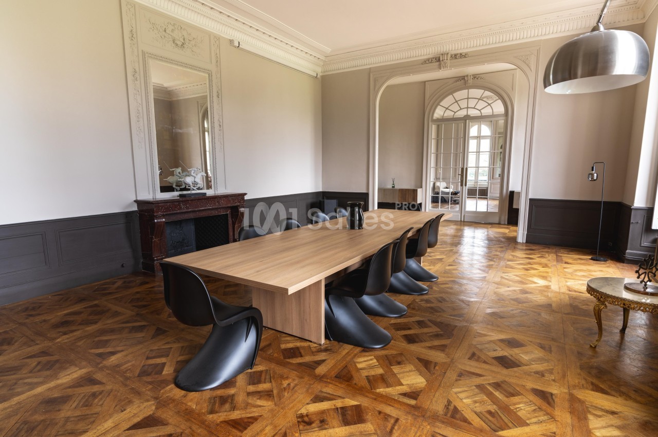 Salle à manger élégante avec table en bois, chaises noires modernes, parquet en chevrons et cheminée décorative.