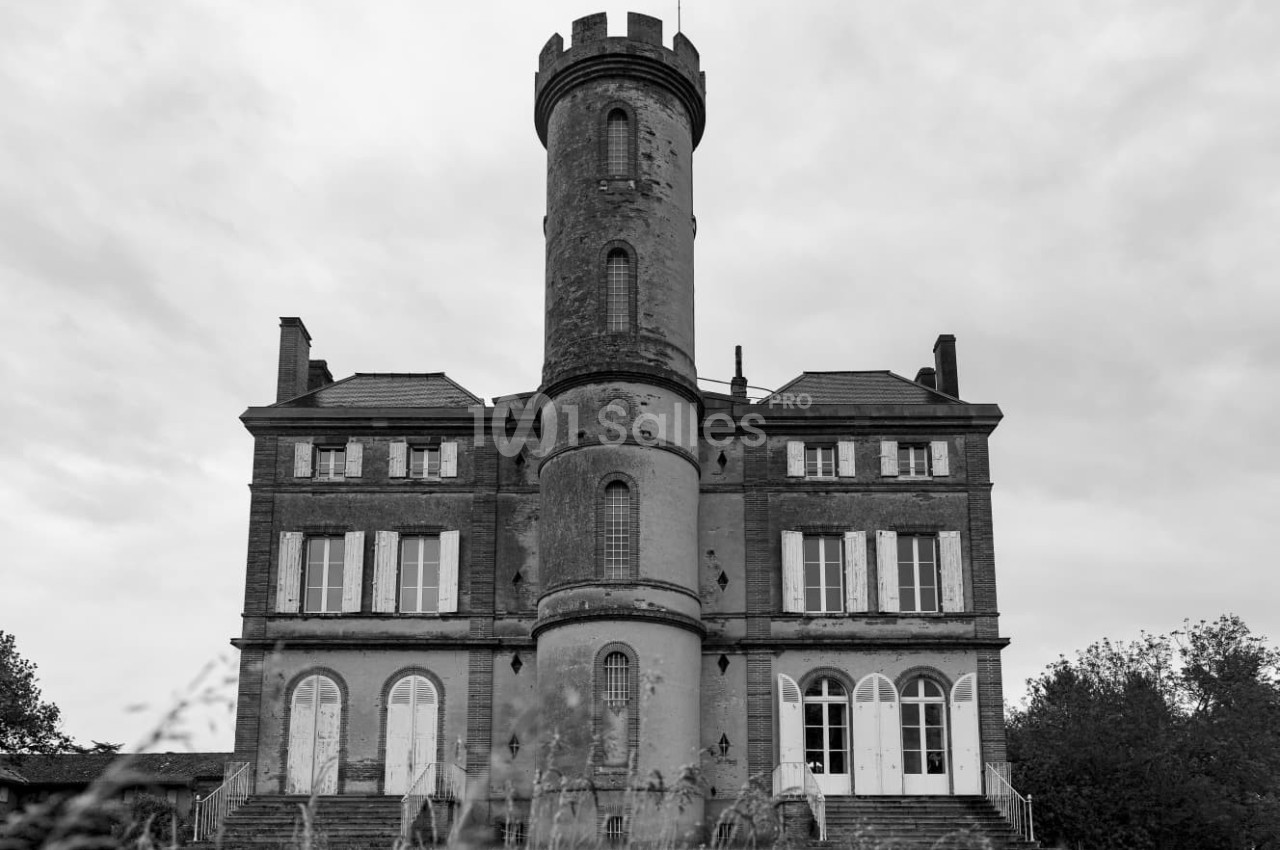 Façade d'un château ancien en briques avec une tour centrale ronde, sous un ciel nuageux.