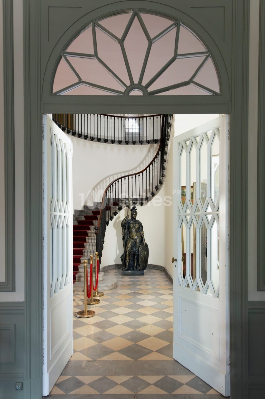 Vue d'une entrée avec portes ouvertes sur un escalier en colimaçon, une statue et un sol en damier.