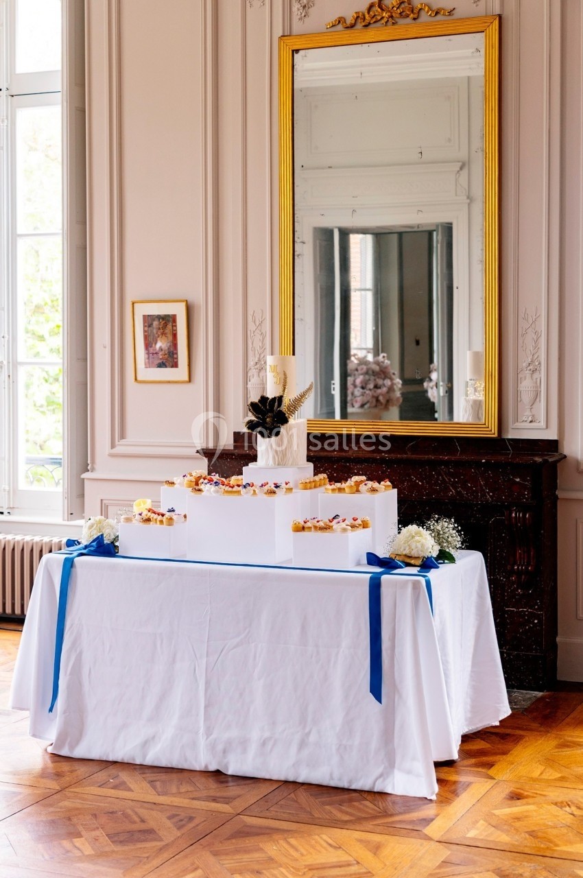 Table décorée avec des boîtes blanches empilées, ornées de rubans bleus et d'un gâteau au sommet, dans une pièce élégante.