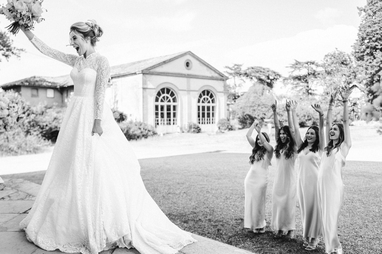 Une mariée brandit son bouquet tandis que quatre demoiselles d'honneur applaudissent joyeusement dans un jardin.