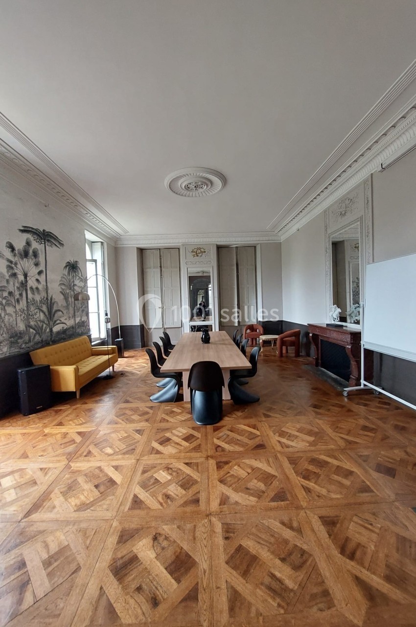 Salle de réunion élégante avec parquet en bois, grande table, chaises noires, canapé jaune et fresque murale tropicale.