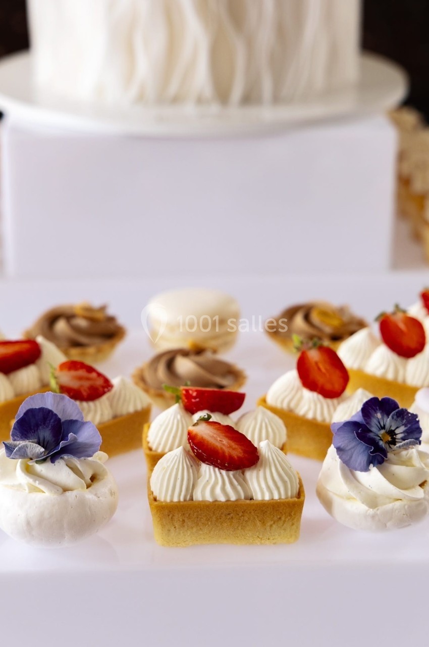 Assortiment de pâtisseries décorées de fraises, fleurs comestibles et crème, avec un macaron en arrière-plan.