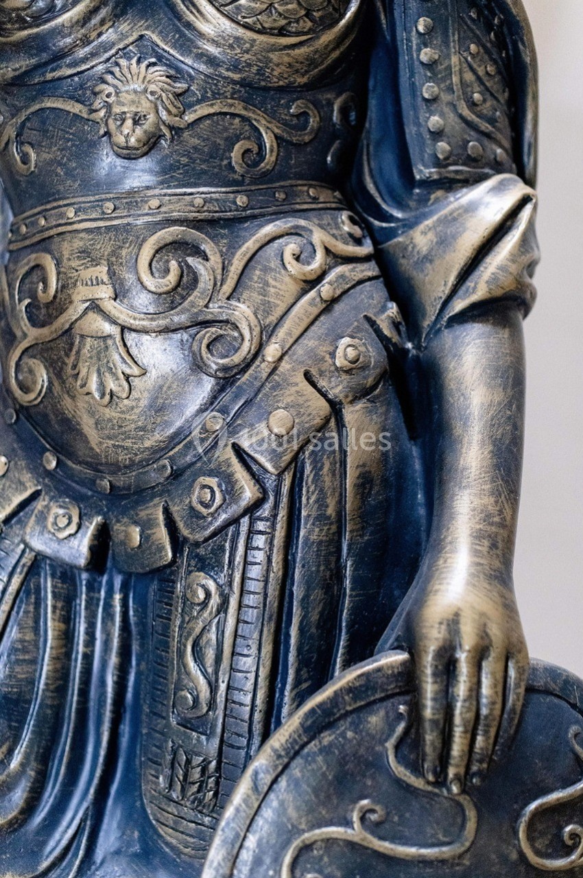 Statue en métal représentant une armure ornée de motifs détaillés, avec une main tenant un bouclier.