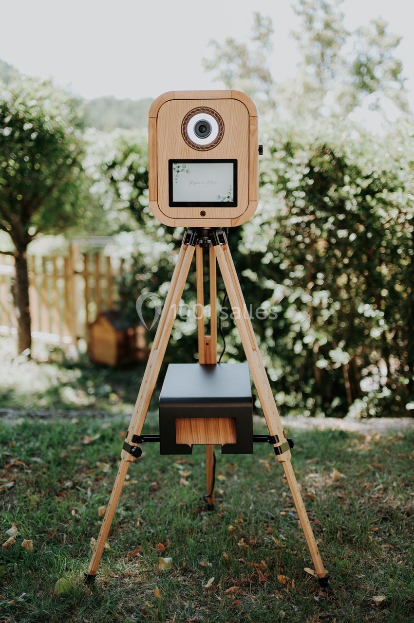 Appareil photo en bois monté sur un trépied, installé dans un jardin avec des arbres en arrière-plan.