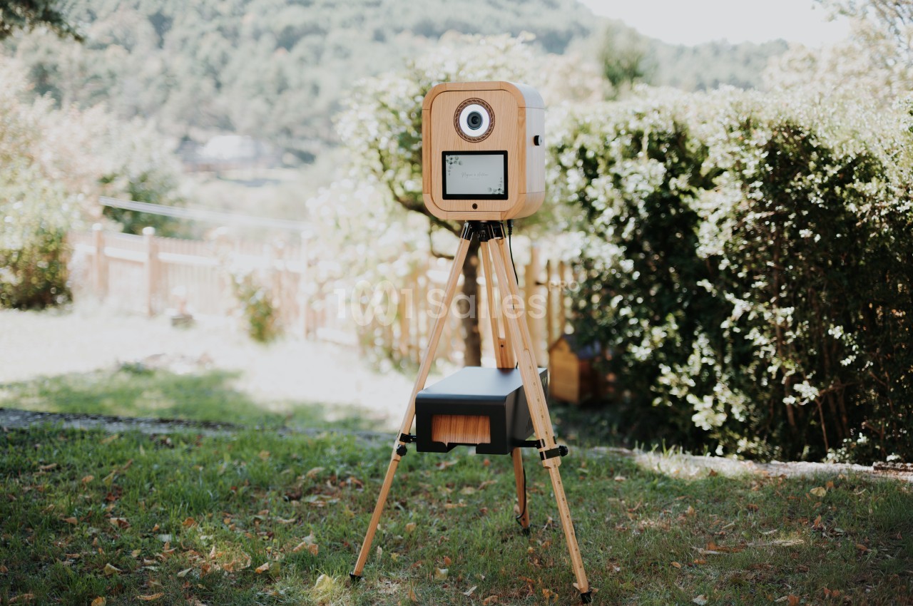 Appareil photo rétro sur trépied en bois installé dans un jardin verdoyant sous un ciel clair.