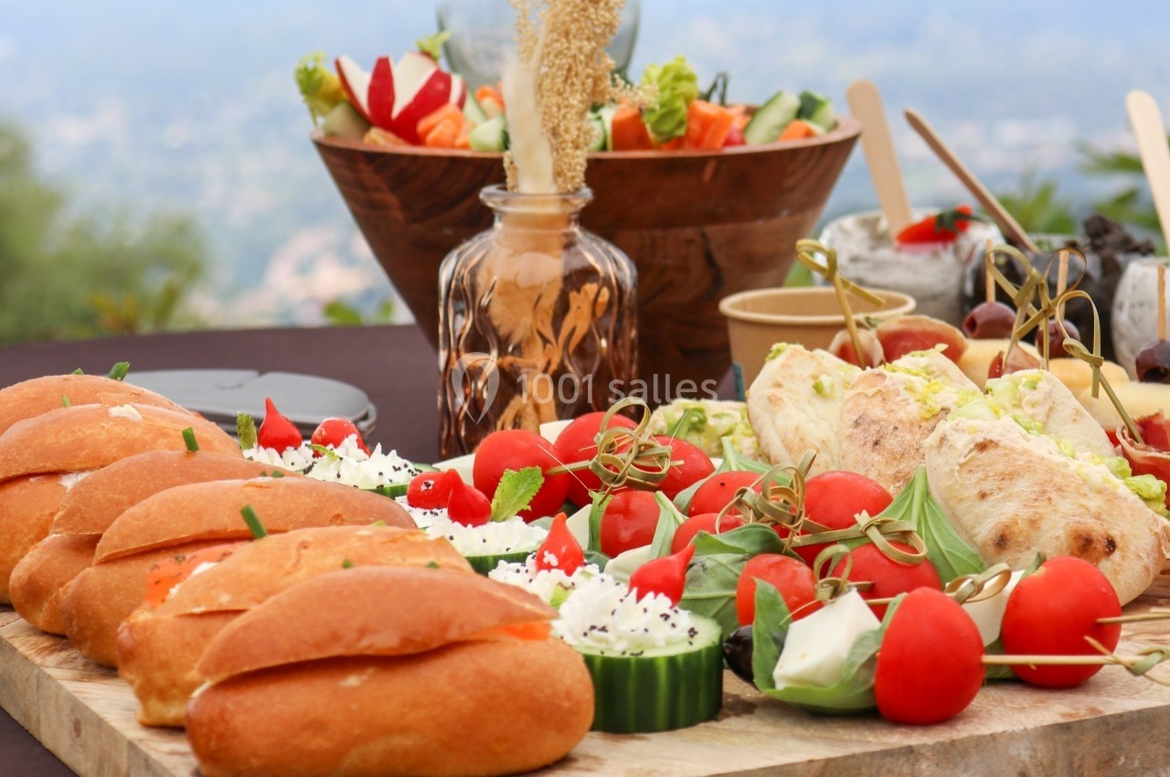Plateau de buffet avec sandwichs, légumes frais, tomates cerises, fromage et desserts en arrière-plan.